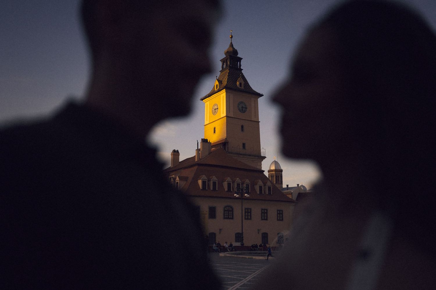A church steeple with illuminated clock tower glows warmly against a dark evening sky.