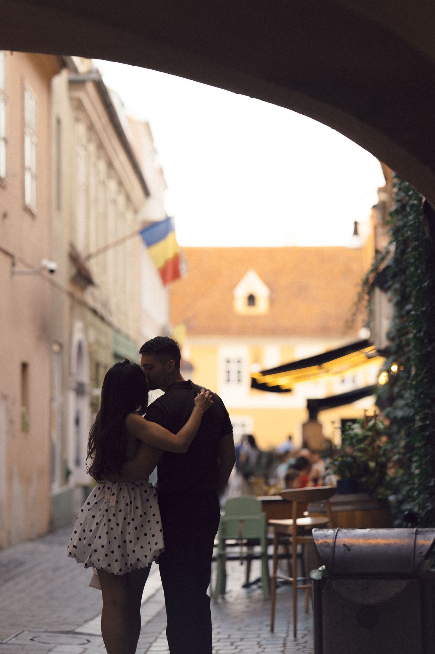 A silhouetted couple embraces in a romantic moment along a charming European street at sunset.