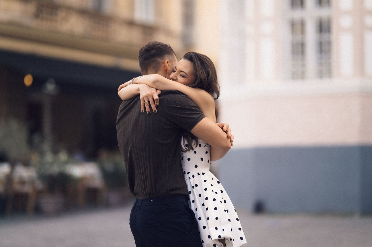 A couple in a romantic embrace wearing black and polka dot clothing dance together in an urban setting.