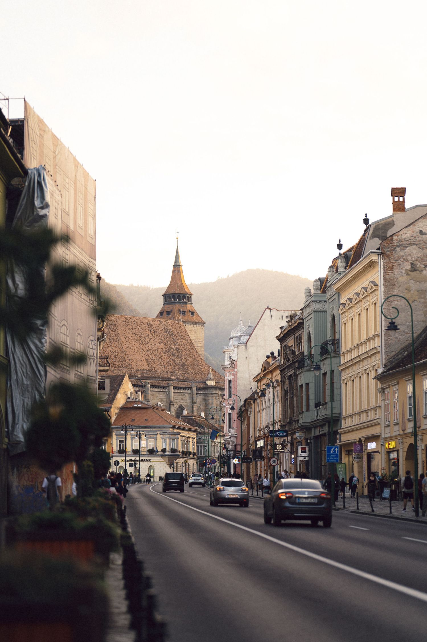 Historic European town street with traditional architecture, church spires, and parked cars along a quiet urban road.