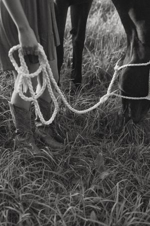 A black and white close-up of cowboy boots and rope leads in grass.
