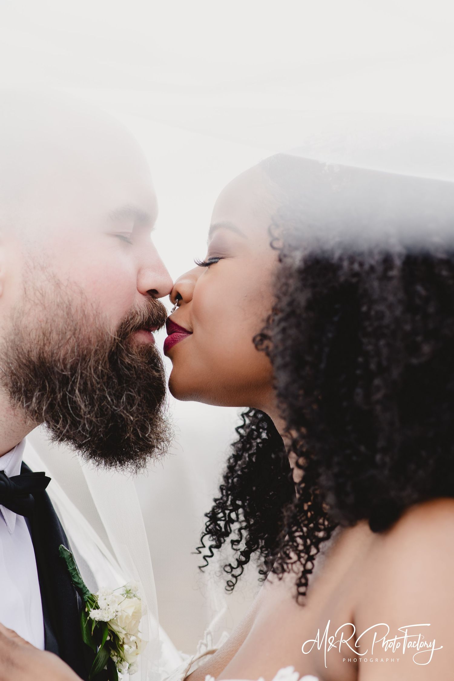 Romantic interracial couple sharing a kiss under a wedding veil on their wedding day.