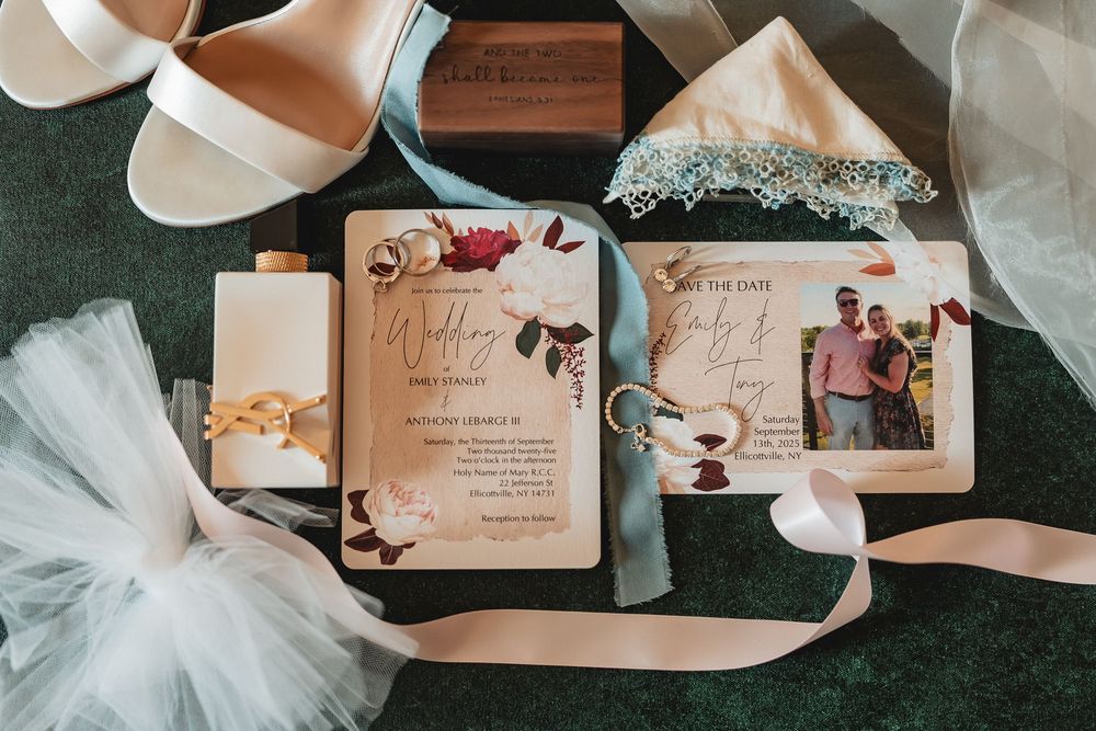 Wedding invitation suite with floral designs, bridal shoes, tulle fabric, and pink silk ribbon laid on green background.