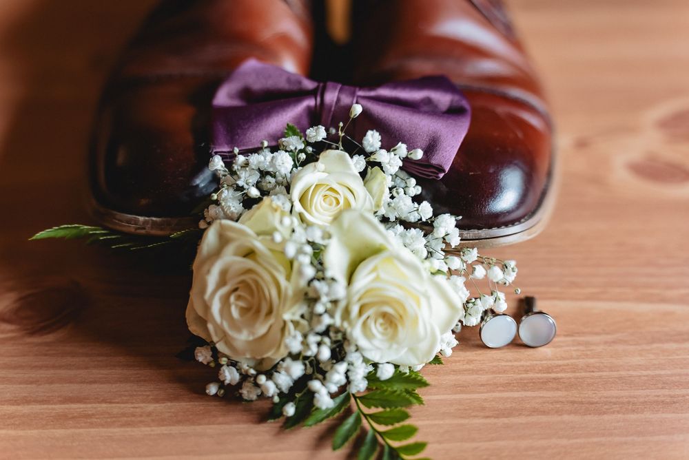 White roses and baby's breath corsage with pearl accents displayed on wooden surface for formal occasion.