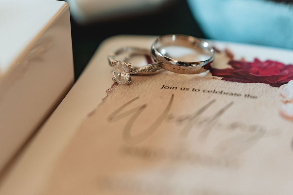 Close-up shot of wedding details including handwritten text and metallic rings on white paper.