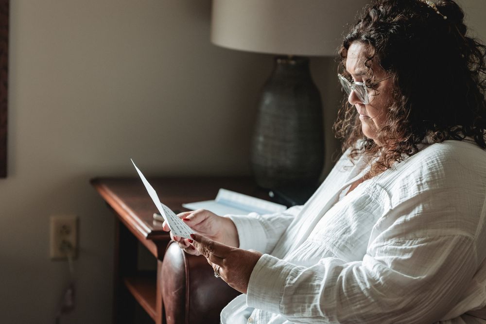 Person in a white robe sits in a chair while using a mobile phone in a dimly lit room.
