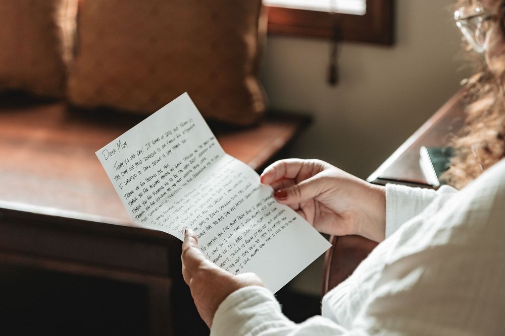 A person writes a handwritten note in elegant cursive script on white paper under warm lighting.