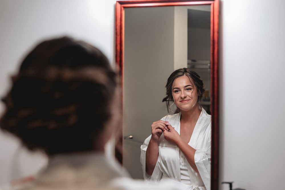 Person in white robe holds coffee mug while looking in bathroom mirror reflection.