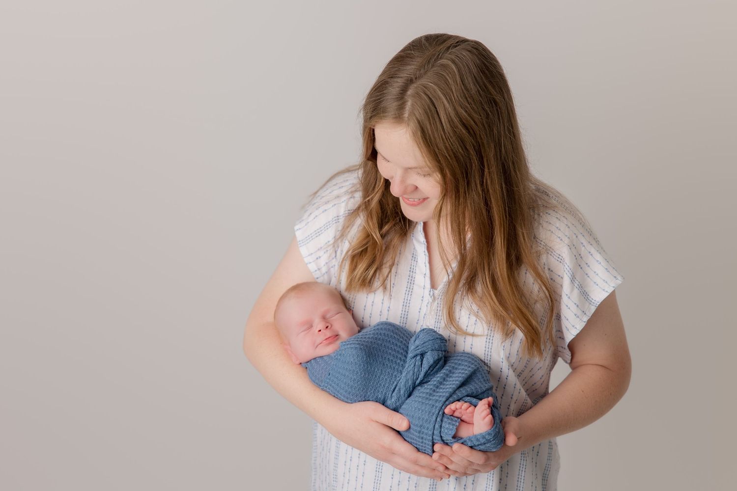 A tender family moment as parents admire their newborn baby against a neutral background.