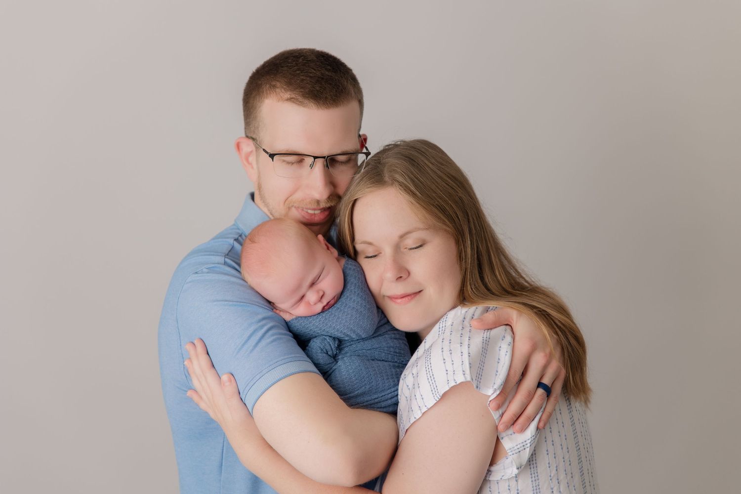 Romantic couple in light blue outfits embrace tenderly against neutral background in photography studio.