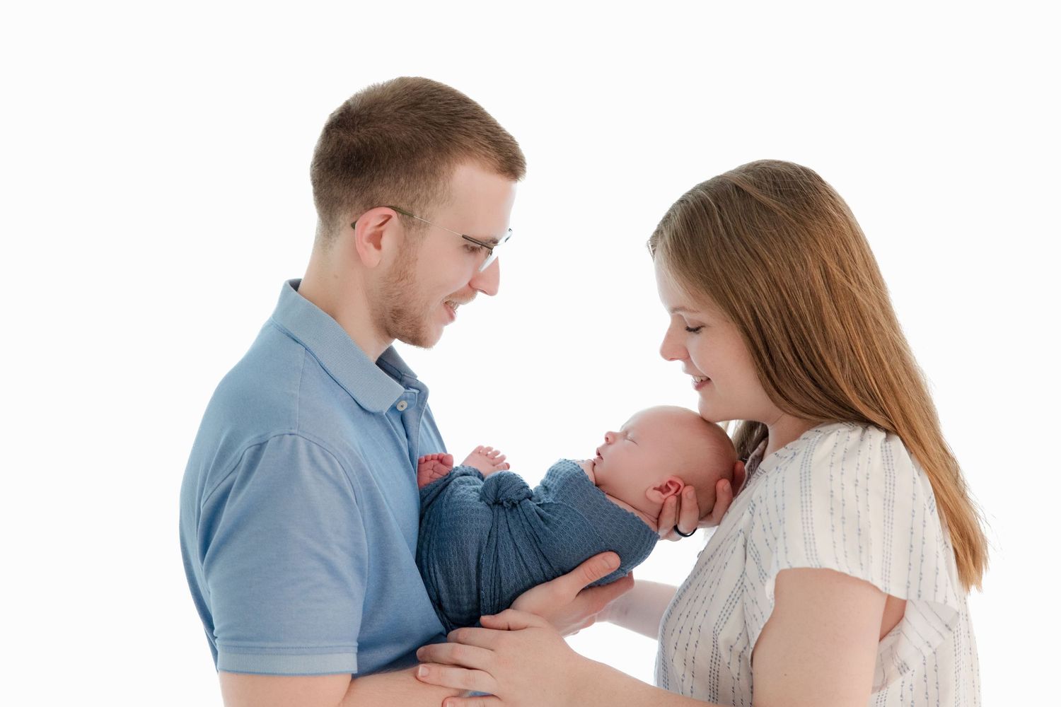 Parents share a loving moment with their infant child in a minimalist portrait setting.