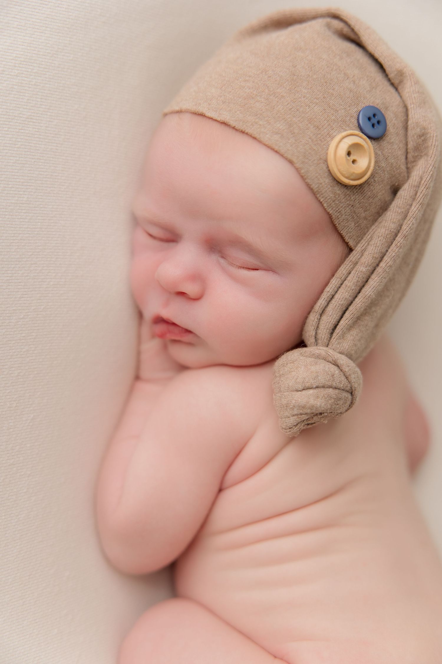 Sleeping newborn wearing tan knit cap with buttons in artistic portrait.
