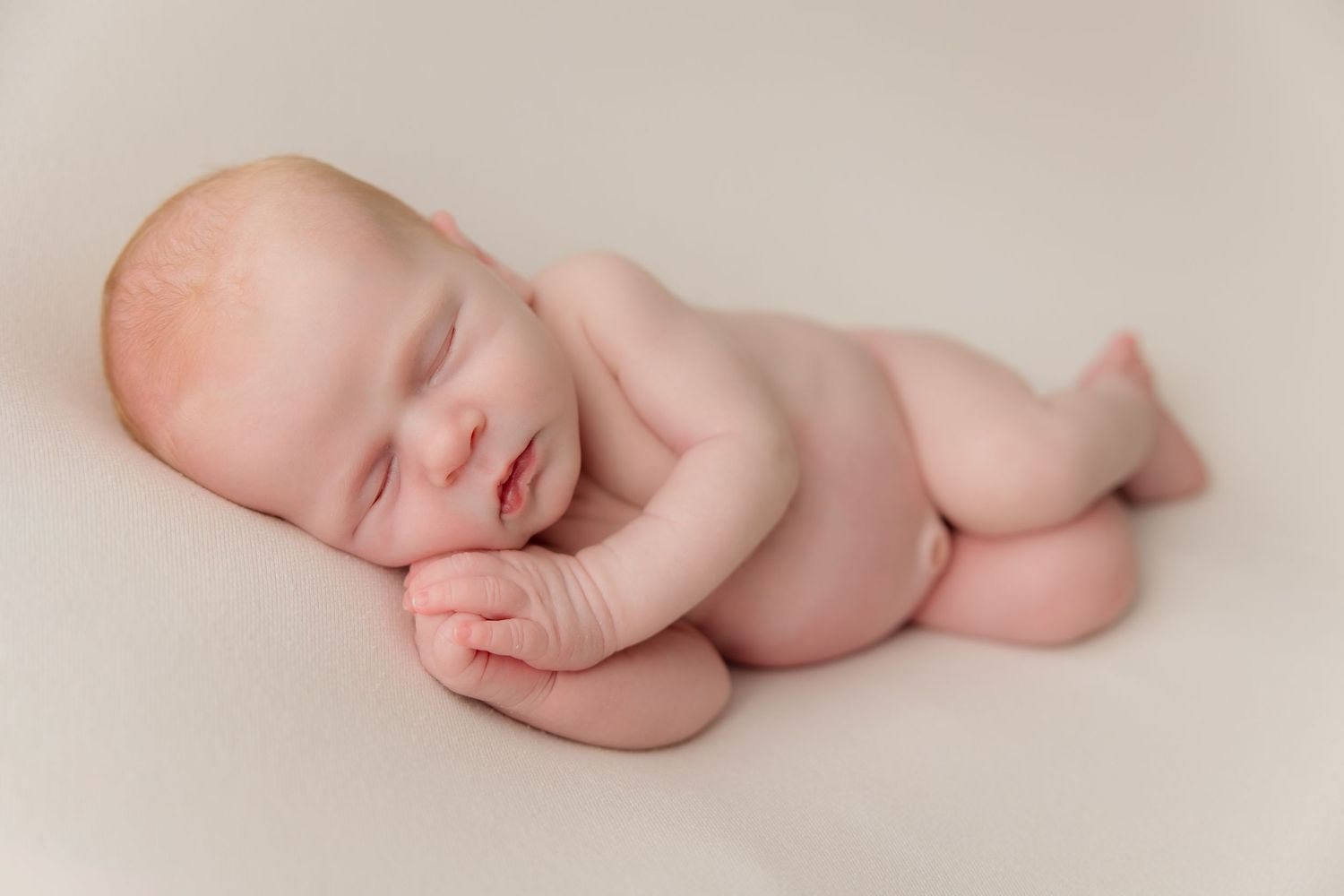 Peaceful sleeping newborn baby lying on soft beige blanket in minimalist portrait setting.
