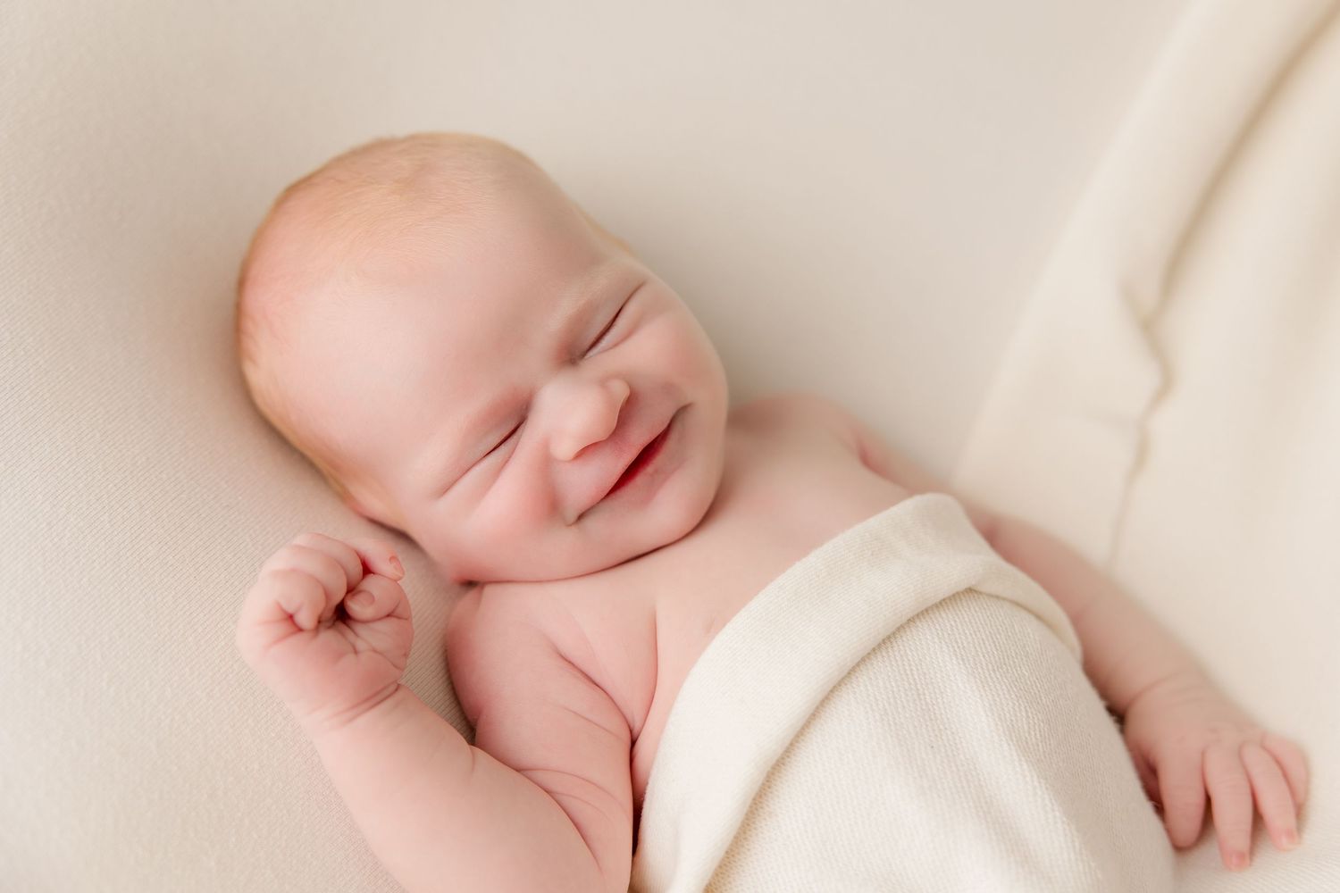Peaceful sleeping newborn on ivory fabric in minimalist portrait style.