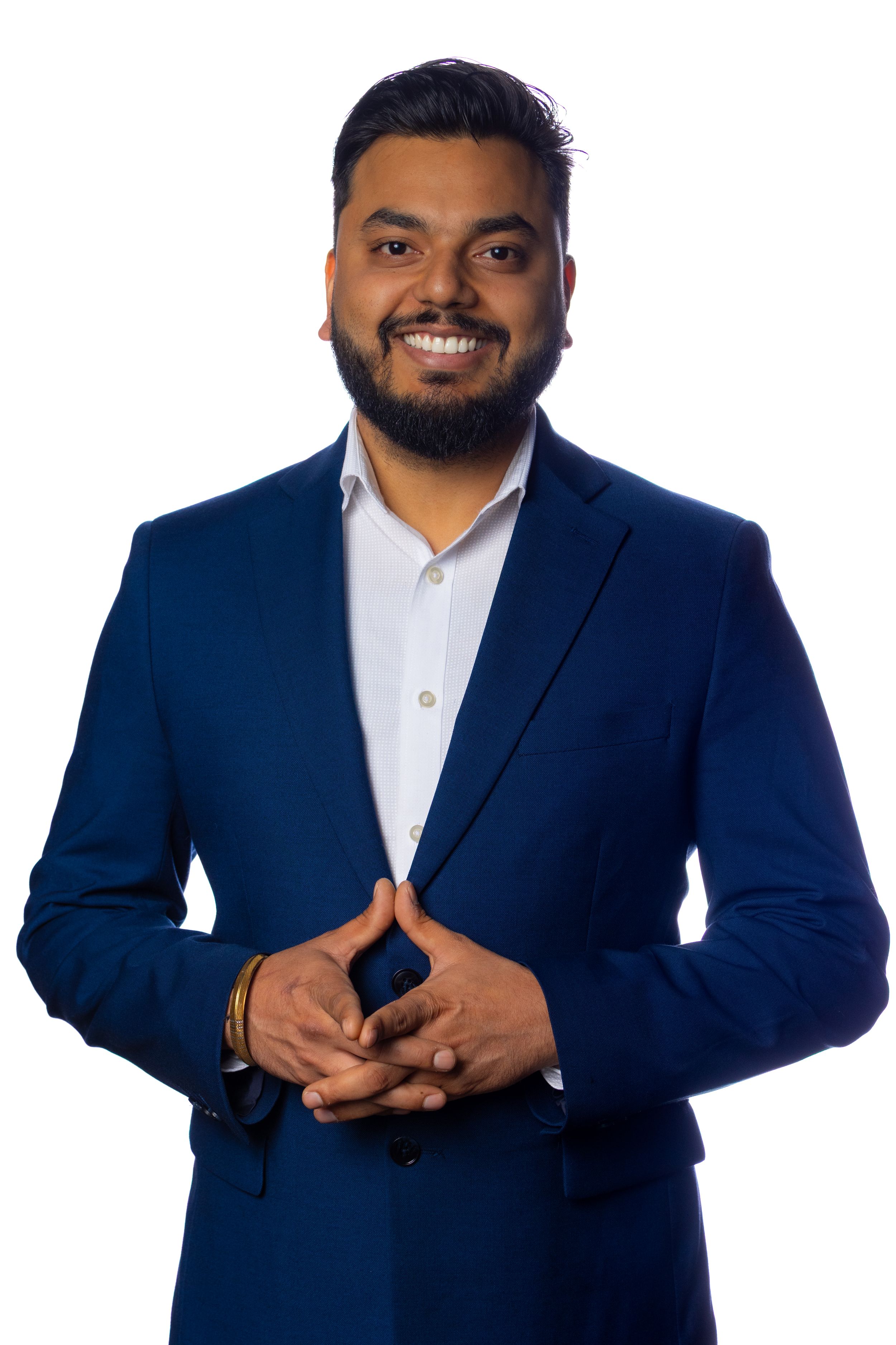 Business professional in a dark blue blazer and white shirt posing with clasped hands against white background.
