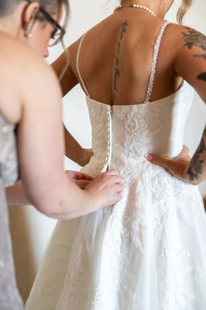 Close-up view of white lace wedding dress details being fastened with buttons down the back.