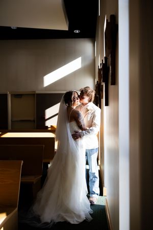 A romantic wedding moment captured in silhouette against bright window light in a hallway setting.