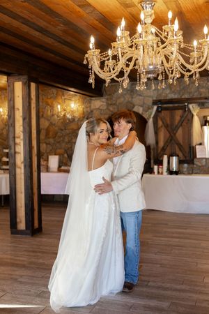 A couple shares their first dance under a crystal chandelier in a rustic barn venue with stone walls.