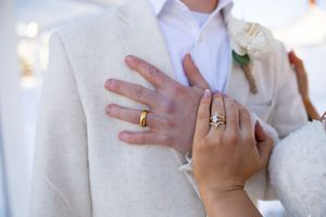 Close up of newlywed couple's hands showing their wedding rings during outdoor ceremony.