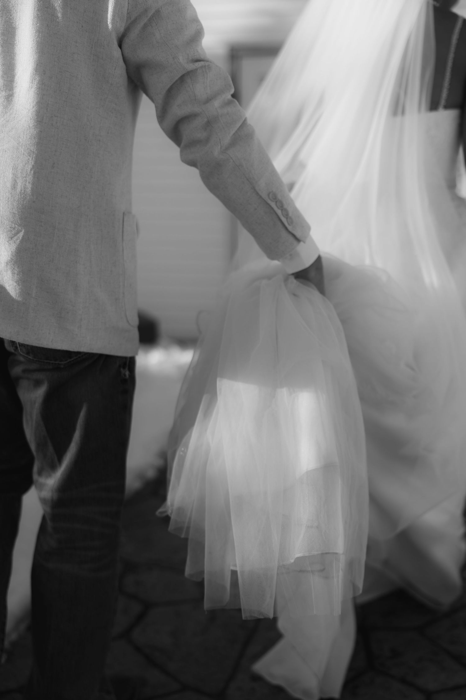 Black and white close-up of a flowing wedding dress train and veil with elegant fabric details.