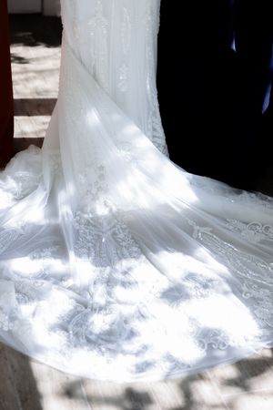 Intricate lace details on the train of a flowing white wedding dress in natural sunlight.