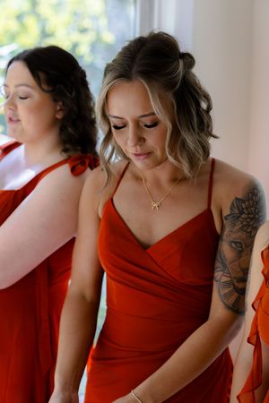 Bridesmaids in vibrant red dresses with elegant styling and visible tattoo artwork.