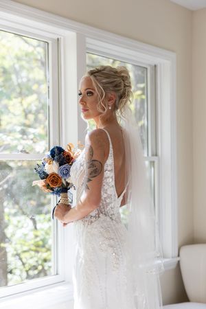 A side profile of a bride in a detailed lace gown holding a blue and peach floral bouquet.