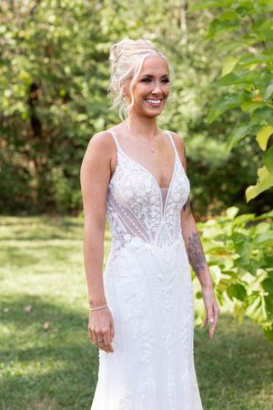 Beautiful lace wedding dress with plunging neckline and delicate details shown in outdoor garden setting.