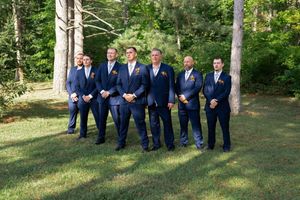 Groomsmen in navy suits pose together on grassy hillside.