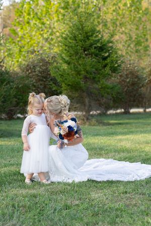 Wedding party with flower girls in white dresses sitting on grass.