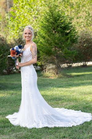 Bride in lace wedding gown with long train poses in garden setting.