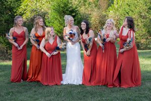 Wedding party with bridesmaids in red dresses gathered on grass.