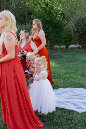 Bridesmaids in red gowns with flower girls in white dresses.