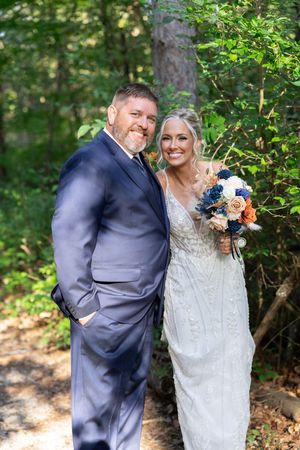 A joyful wedding couple shares laughter among blooming trees and natural scenery.
