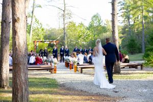 Outdoor wedding ceremony setup with wooden benches among pine trees.
