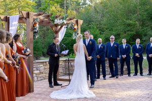 Wedding party lined up during outdoor ceremony with bridesmaids in rust-colored dresses.