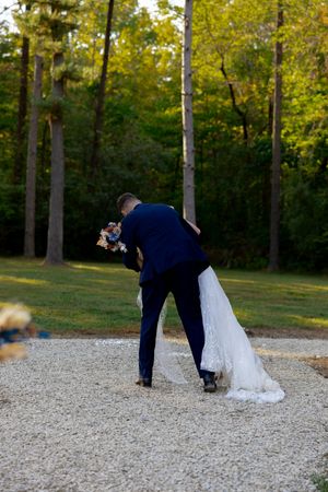 Wedding couple walking along gravel path surrounded by tall pine trees.