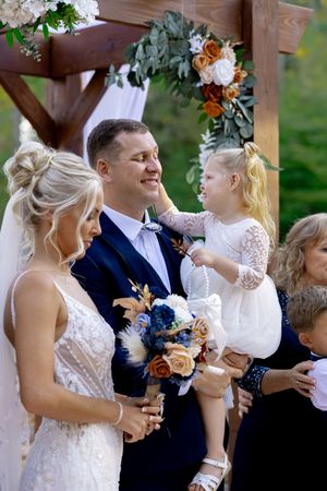 Wedding party gathered under wooden pergola decorated with flowers.