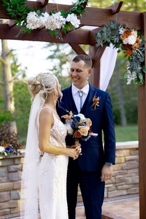 Couple shares moment under floral-decorated wooden pergola during wedding ceremony.