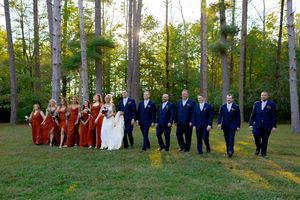 Wedding party lineup in forest setting with bridesmaids in rust dresses and groomsmen in navy suits.