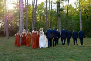 Wedding party silhouetted against sunset in wooded setting.