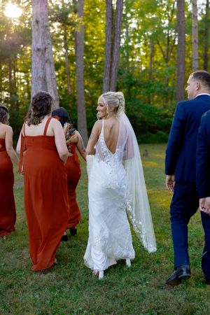 Wedding party walking together outdoors with sunset light filtering through trees.