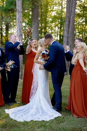 Joyful wedding party celebration in forest setting with orange and navy color scheme.
