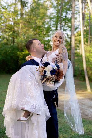 Romantic wedding moment with white lace dress and navy suit in outdoor forest setting.