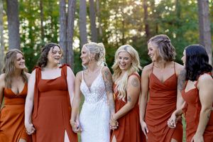 Wedding party in burgundy dresses and navy suits poses together in a wooded outdoor setting at sunset.