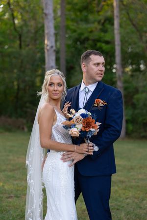 Wedding couple shares intimate moment while holding bouquet in outdoor forest setting.