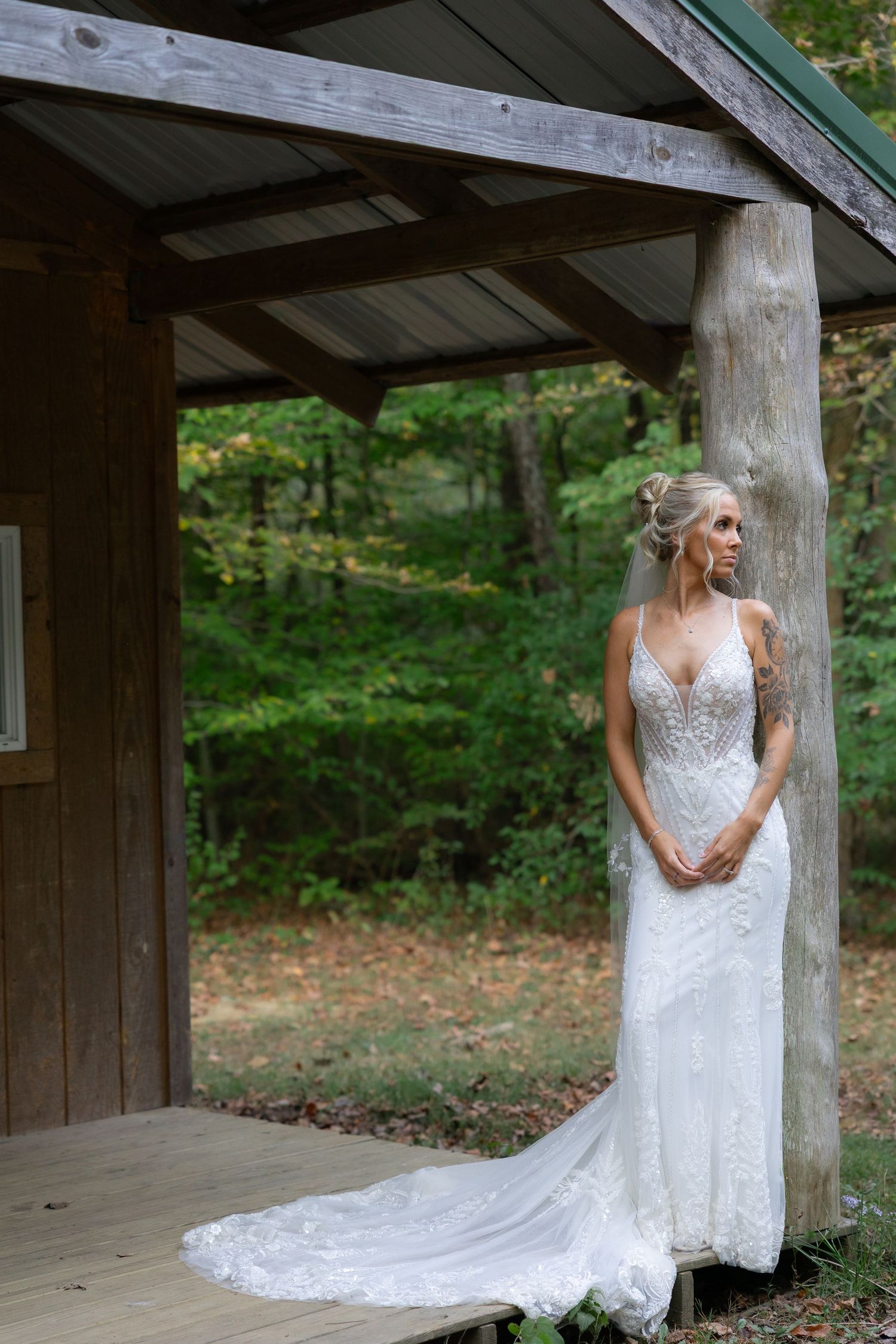 A white lace wedding dress with a long train is showcased on a rustic wooden porch.