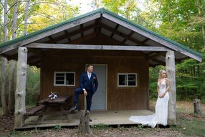 A rustic wooden cabin serves as a backdrop for wedding photography in a forest setting.