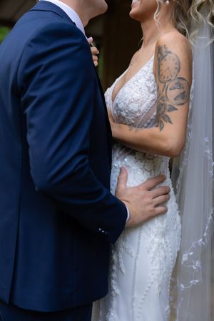 Close-up details of a white lace wedding dress and navy suit during an intimate moment.