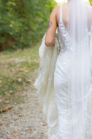 The intricate lace details of a flowing white wedding dress trail behind on a forest path.